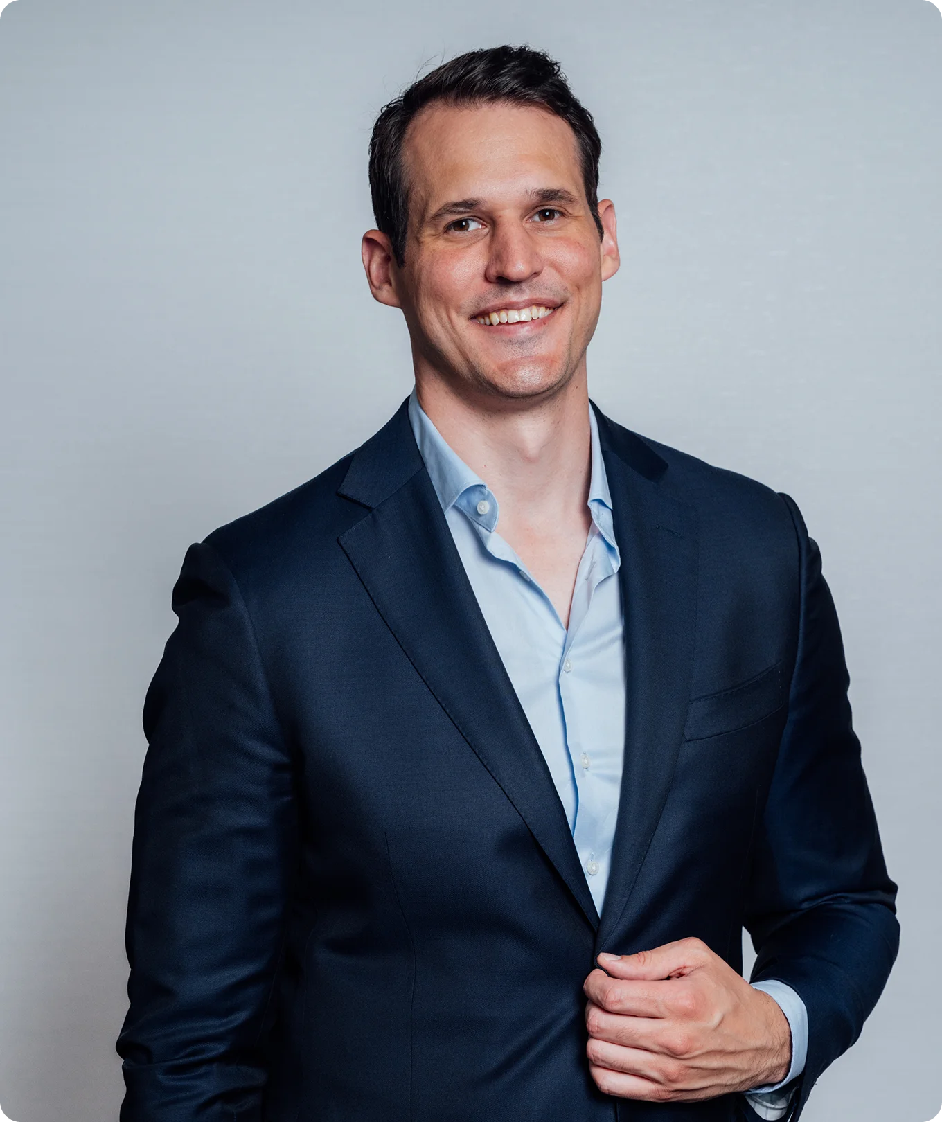 Dr Peter Swiatek MD in navy blue suit and light blue shirt smiling at camera against gray background - Doctor in Carmel, IN