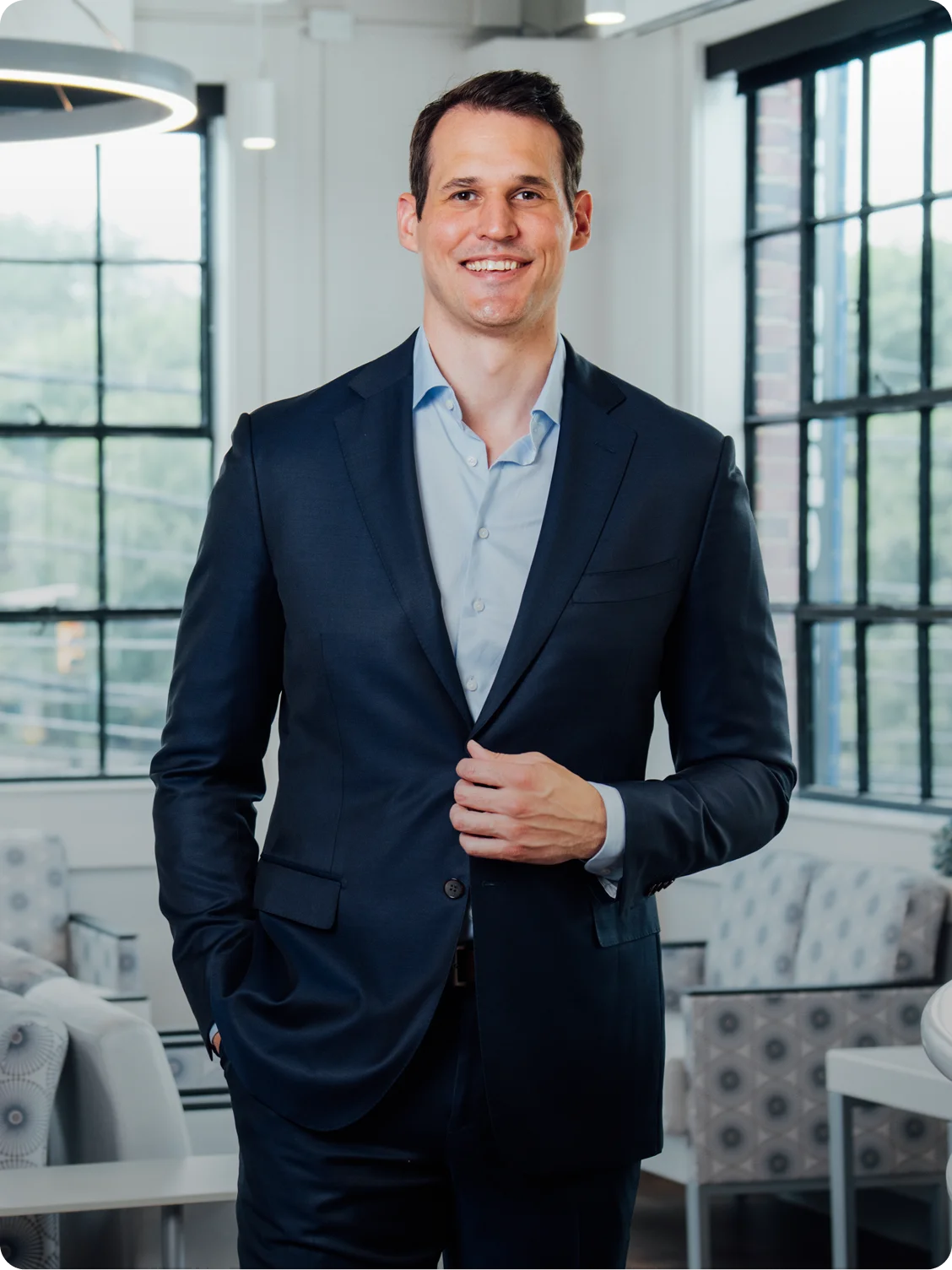 Dr Peter Swiatek MD in navy suit smiling in modern office with industrial windows and contemporary furniture - in Carmel, IN