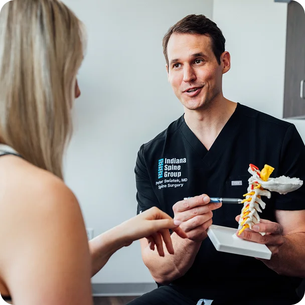 Dr Peter Swiatek MD explaining spine anatomy to patient using anatomical model during consultation - in Carmel, IN