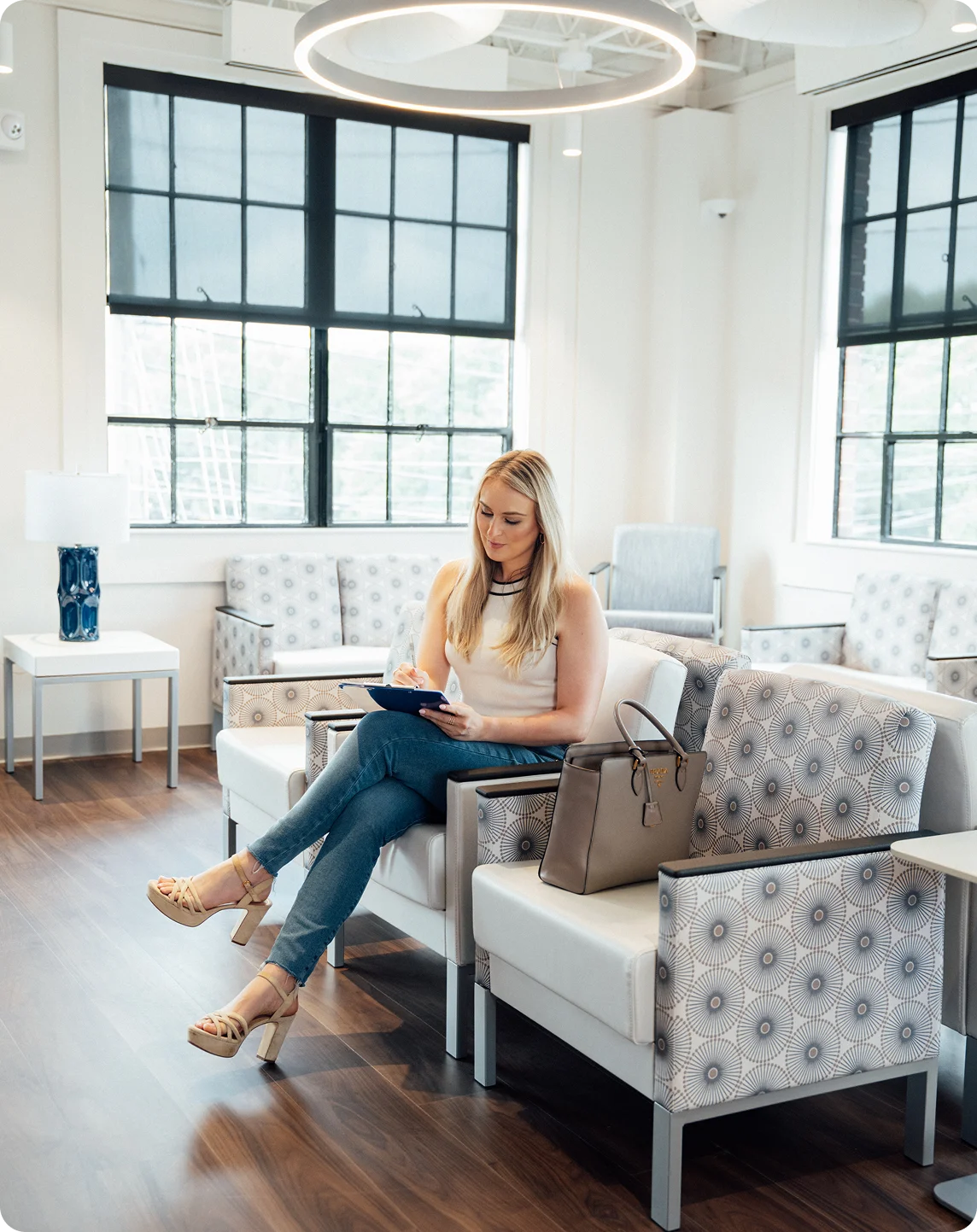 Woman working on laptop in modern bright office waiting room with white furniture and large windows - in Carmel, IN