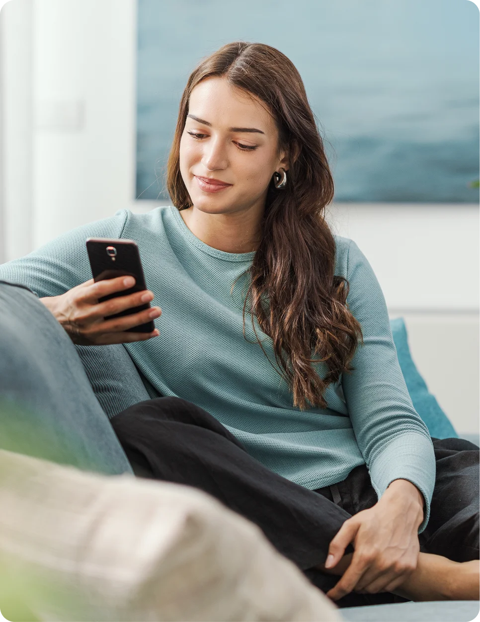 Woman in blue sweater relaxing on couch while using smartphone at home - in Carmel, IN