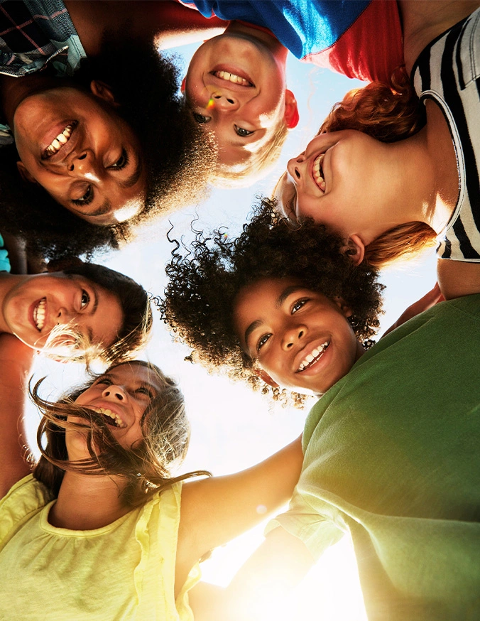 Diverse group of smiling young people in circle looking down at camera with bright sky background - Adolescent idiopathic scoliosis in Carmel, IN