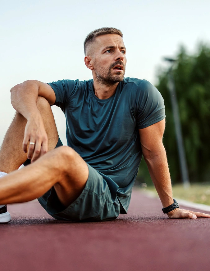 Man in athletic wear sitting on yoga mat outdoors during fitness workout or stretching session - Adult degenerative scoliosis in Carmel, IN