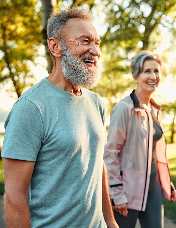 Active senior couple walking outdoors in sunny park during autumn, smiling and enjoying healthy lifestyle - Corpectomy in Carmel, IN