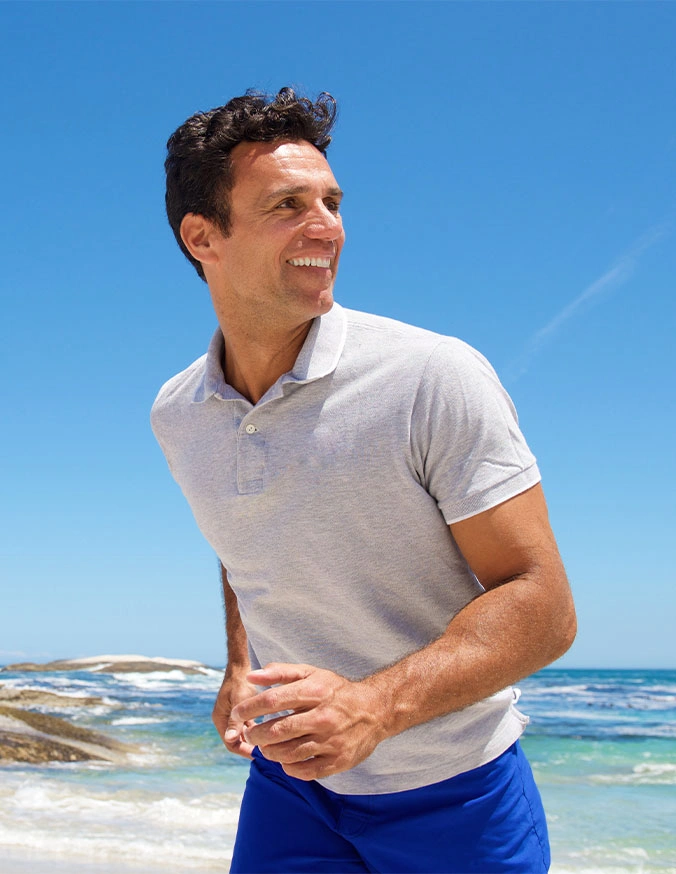 Man in white polo shirt smiling at beach on sunny day with blue ocean background - Failed back surgery in Carmel, IN
