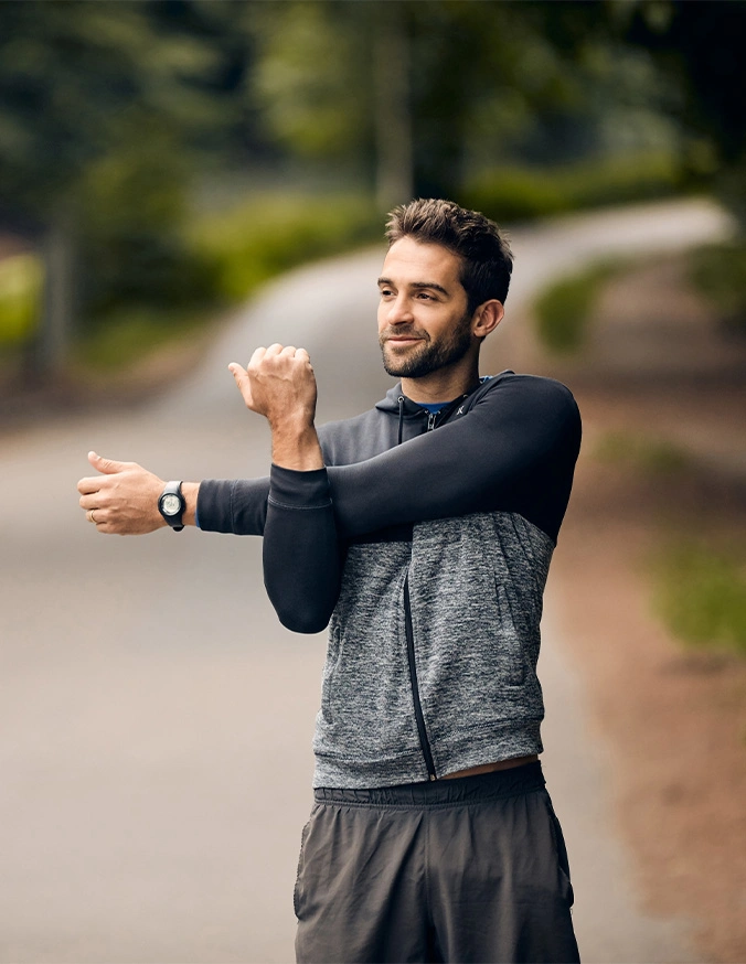 Man stretching arm across chest during outdoor workout warmup on path in athletic wear - Lumbar fractures in Carmel, IN