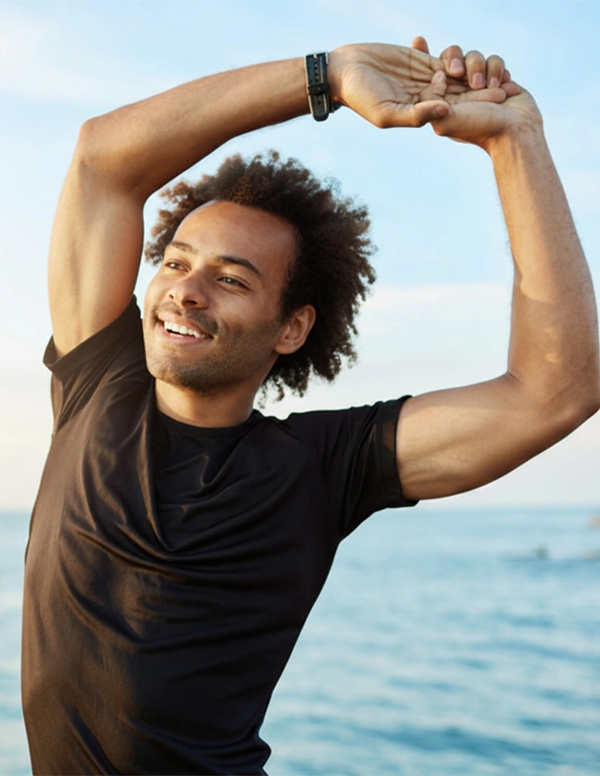 Young man stretching outdoors by the ocean, smiling while doing side bend exercise in athletic wear - Lumbar radiculopathy in Carmel, IN