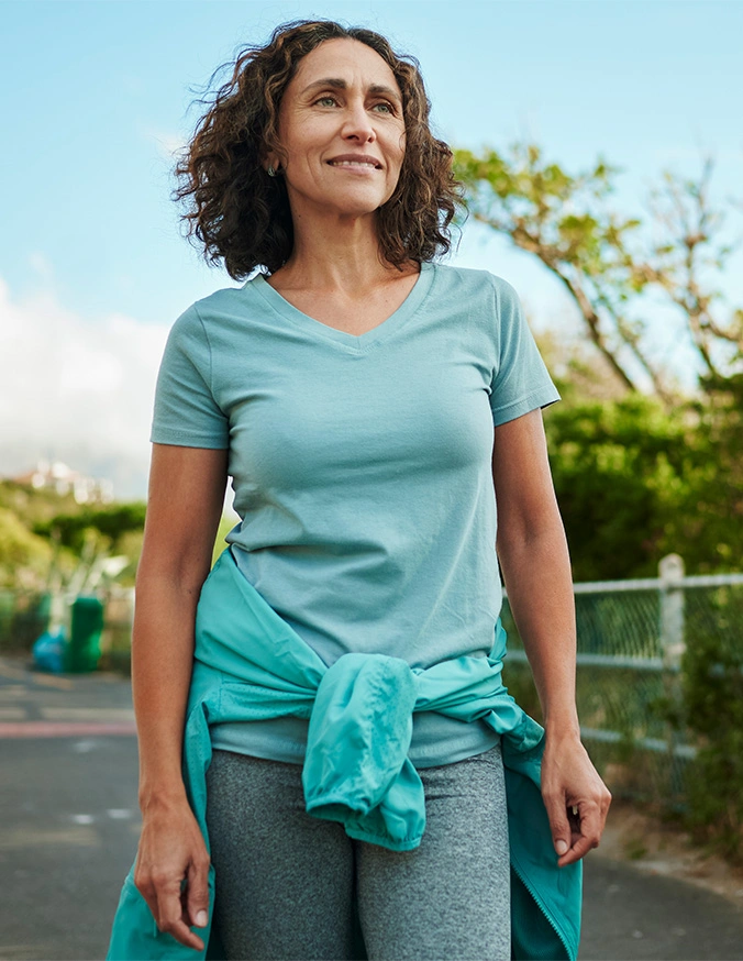 Woman in blue athletic shirt with jacket tied around waist standing outdoors on tennis court - Lumbar Spondylolisthesis in Carmel, IN