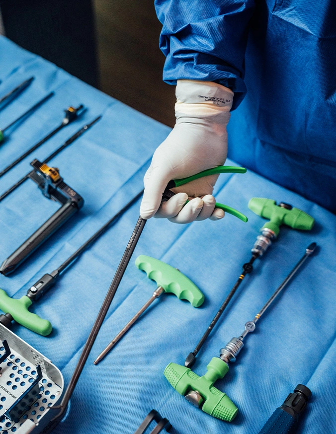 Surgeon's gloved hand selecting green surgical instruments from sterile tray during medical procedure - PSO in Carmel, IN