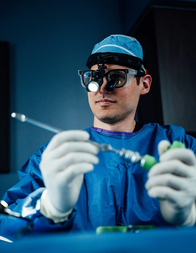 Dr Peter Swiatek wearing protective glasses performing minimally invasive procedure with surgical instruments in operating room - PTDF in Carmel, IN