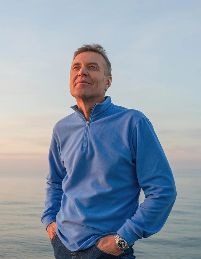 Man in blue pullover standing by ocean at sunset looking upward thoughtfully - Thoracic disc herniations in Carmel, IN