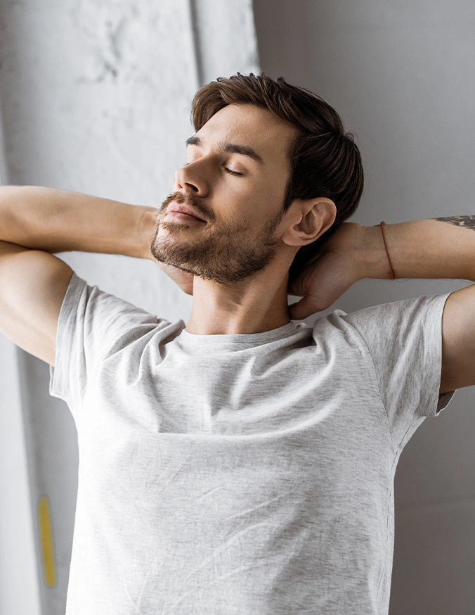Man relaxing with hands behind head, eyes closed, wearing white t-shirt in peaceful moment of rest and meditation - Ervical radiculopathy in Carmel, IN